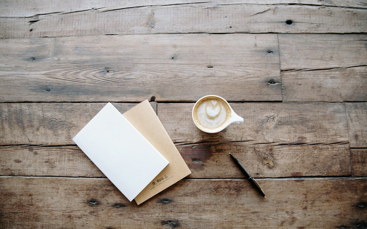 An open notebook and a cup of coffee on a wooden table.