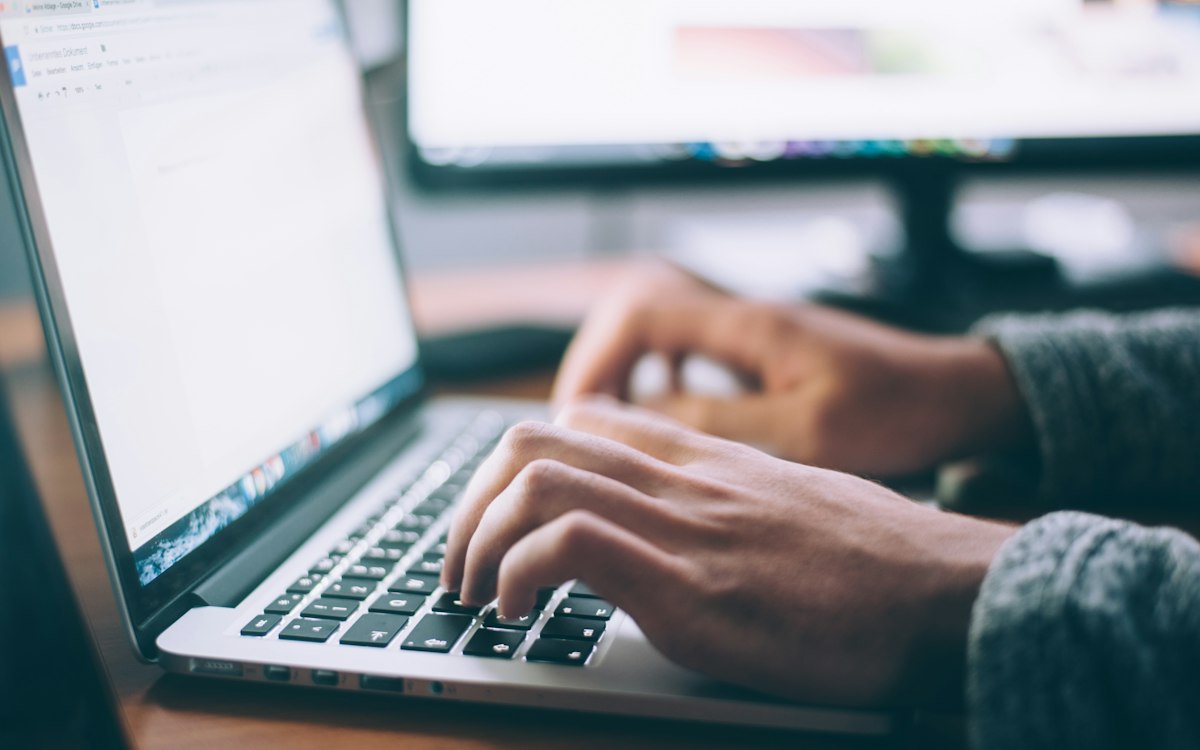 Hands typing on a laptop beside an open notebook.