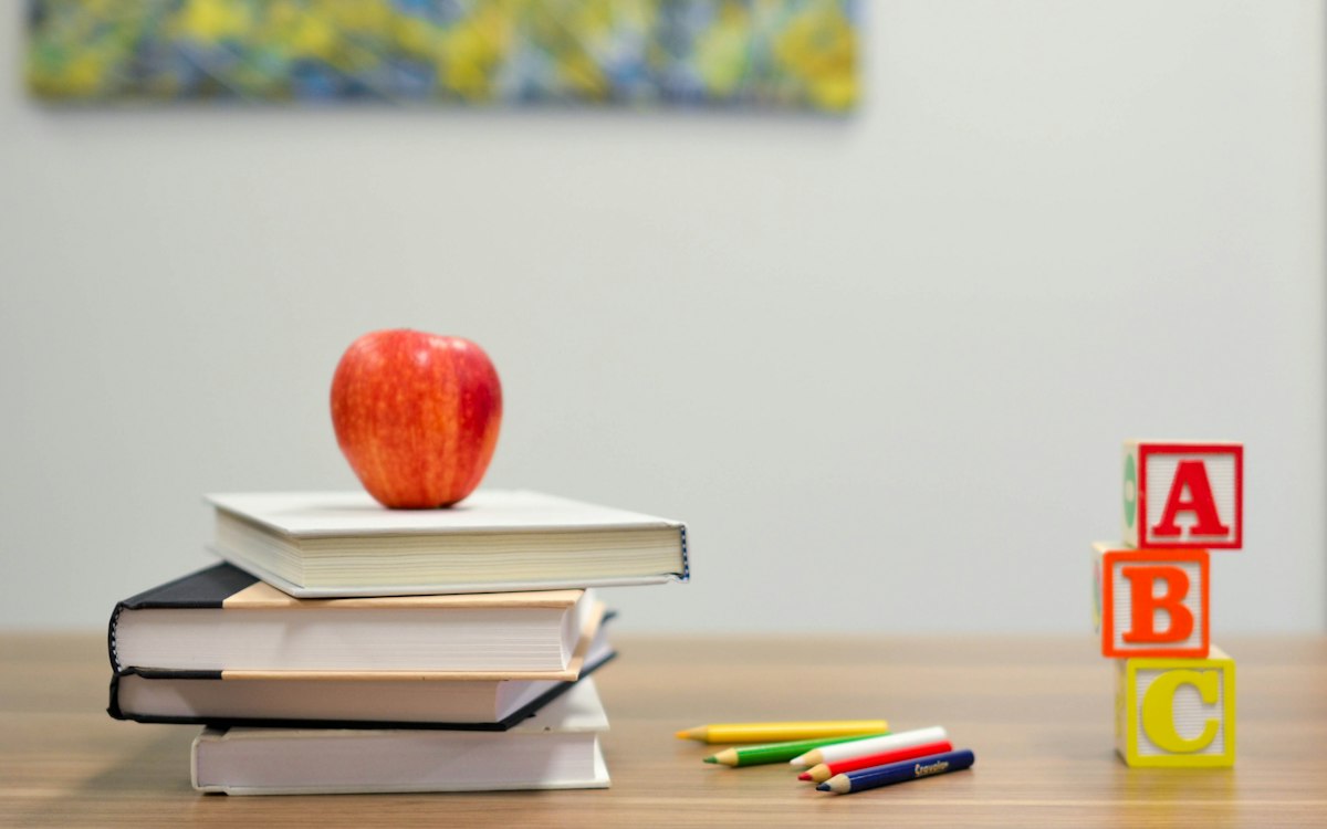 A stack of books and an apple beside colorful letter blocks.