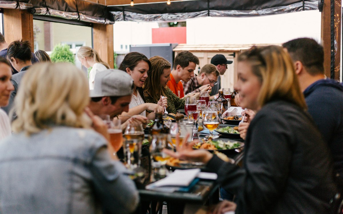 Friends talking over a meal at a long outdoor table.