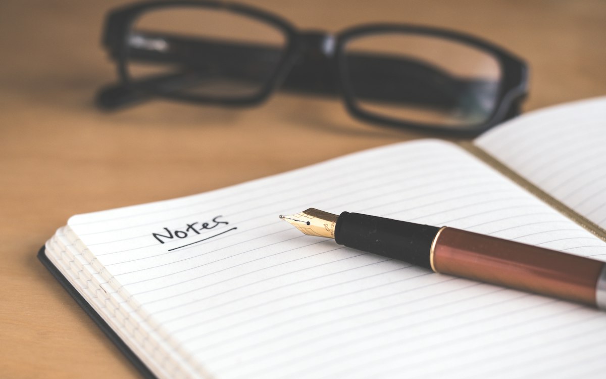 An open notebook labeled Notes beside a pen and reading glasses.