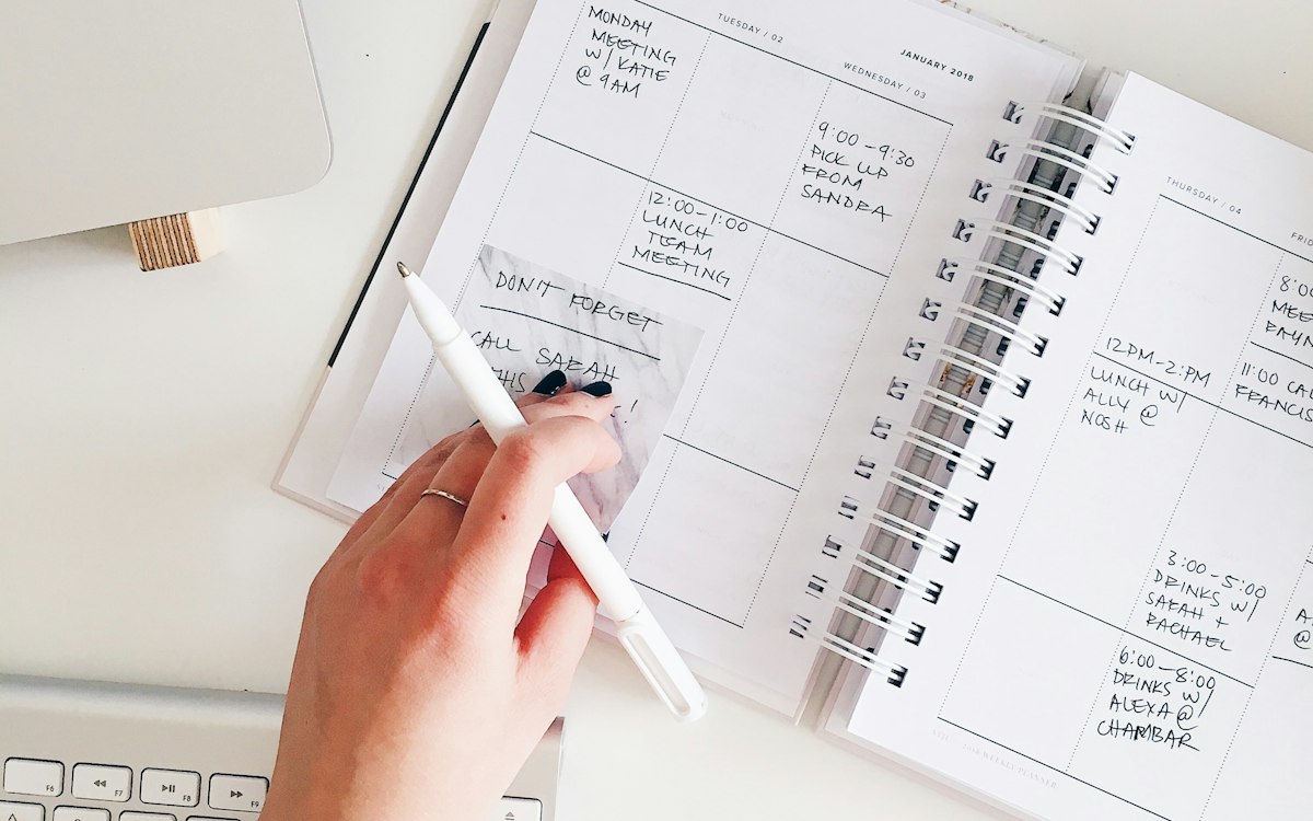 A hand writing in an open weekly planner.