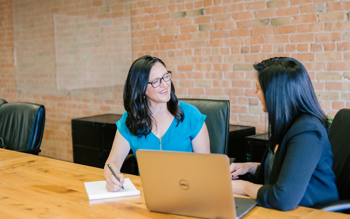 Two colleagues talking across a table with a laptop.