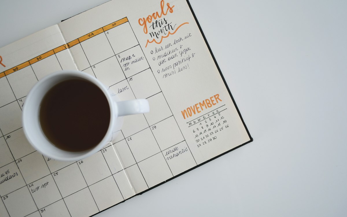 An open calendar and a cup of coffee on a desk.