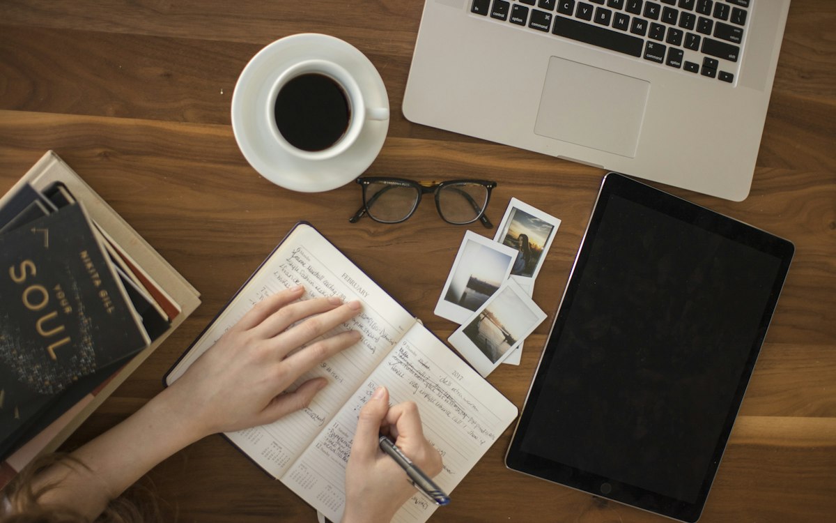 A person sketching and planning beside a laptop and coffee.