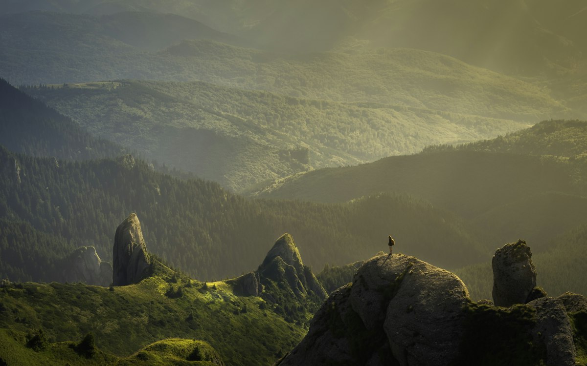 A small figure standing among rocky mountain peaks.