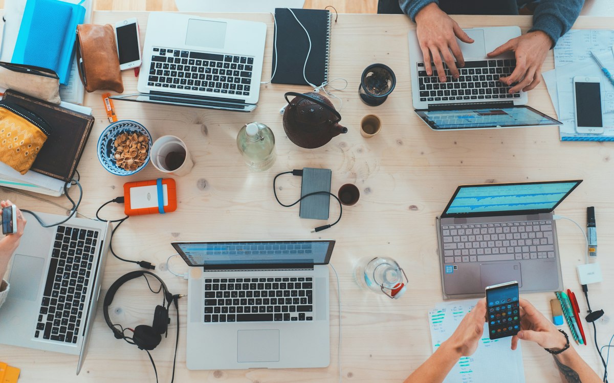 A shared worktable with laptops and colleagues’ hands.