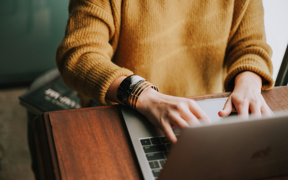 A person in a mustard sweater working on a laptop.
