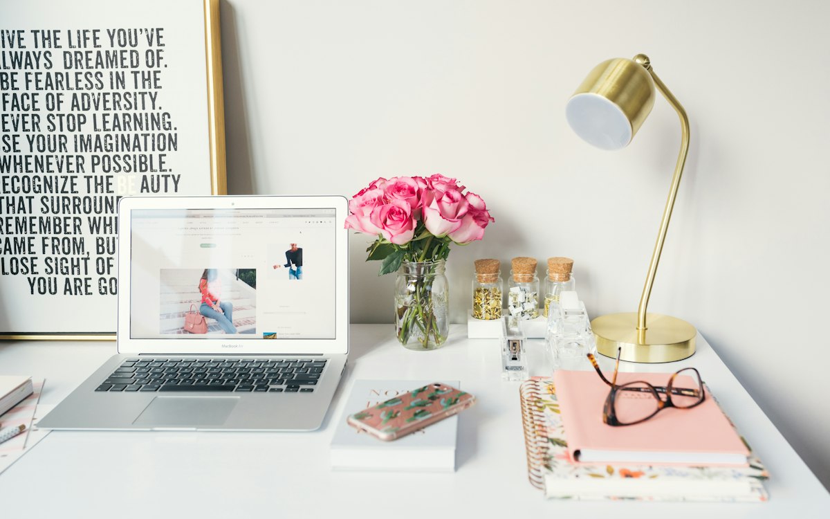 A bright workspace with a laptop, flowers and stationery.