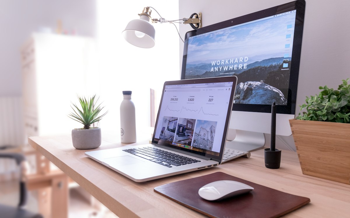 A laptop and monitor in a sunlit home workspace.